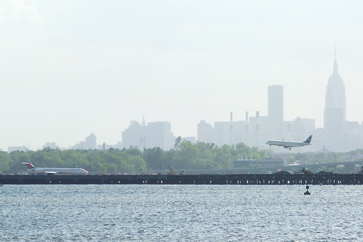 View of Airpline flying past Manhattan Skyline from Hermon A. Macneil Park in College Point