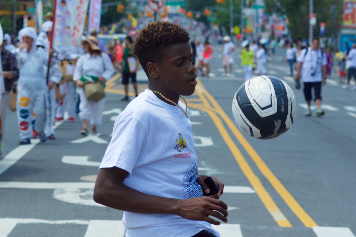 Kid kicking a soccer ball along the Silleteros parade route in Jackson Heights, Queens